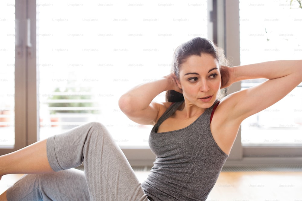 Beautiful young woman working out at home in living room, doing yoga or pilates exercise. Woman doing abdominal crunches.