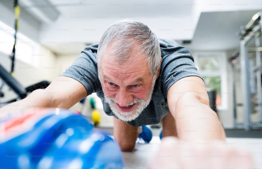 Uomo anziano in abbigliamento sportivo in palestra che si esercita con rullo a ruota per addominali a terra come parte dell'allenamento fitness.