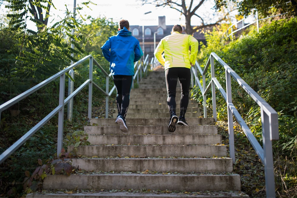 Two young athletes running on stairs outside in sunny autumn nature. Trail runners training for cross country race. Rear view.