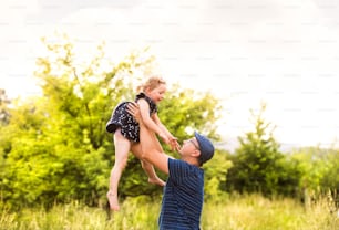 緑の夏の自然の中で、かわいい娘を空高く抱っこする若い父親。