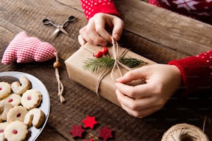 알아볼 수 없는 여자의 손이 크리스마스 선물을 감싸고 장식하고 나무 테이블 배경에 놓여 있다. 스튜디오 촬영.