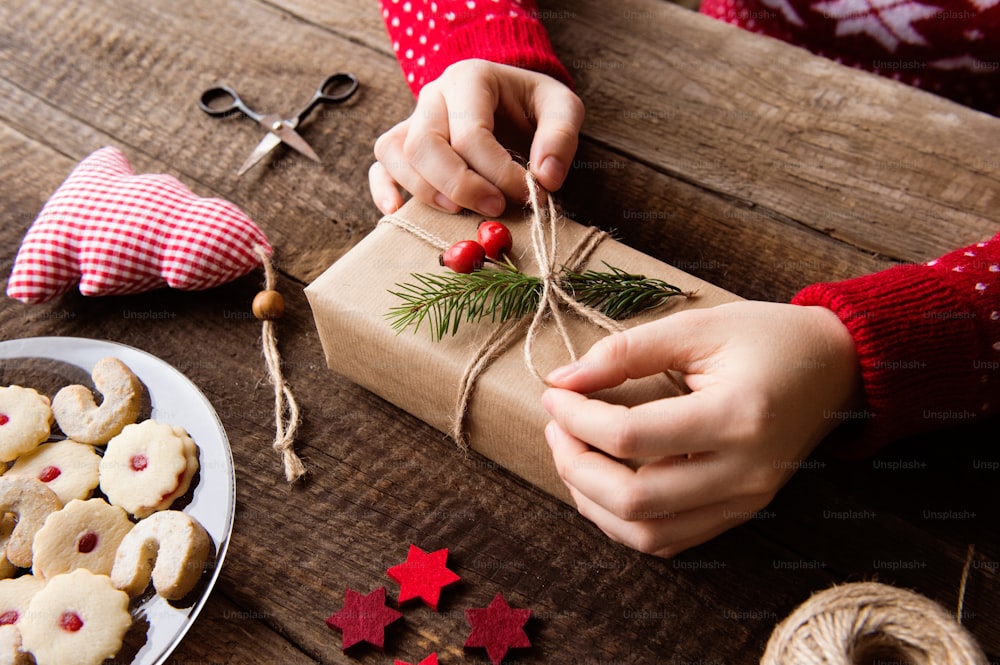 Hands of unrecognizable woman wrapping and decorating Christmas present laid on a wooden table background. Studio shot.