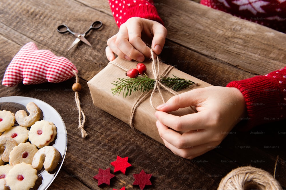 Hände einer nicht erkennbaren Frau, die Weihnachtsgeschenke einwickeln und dekorieren, liegen auf einem Holztischhintergrund. Studioaufnahme.