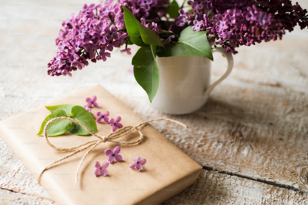 Bellissimo bouquet lilla viola in vaso posato sul tavolo e presente avvolto in carta marrone. Scatto in studio su sfondo di legno bianco.