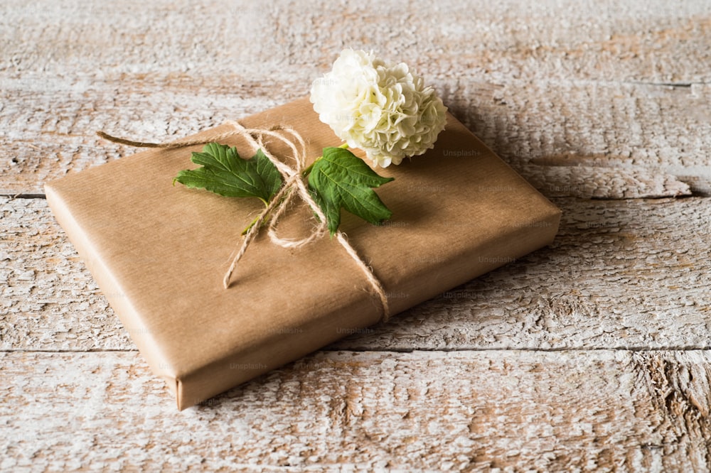 Present wrapped in brown paper decorated by lilac flower. Studio shot on white wooden background.