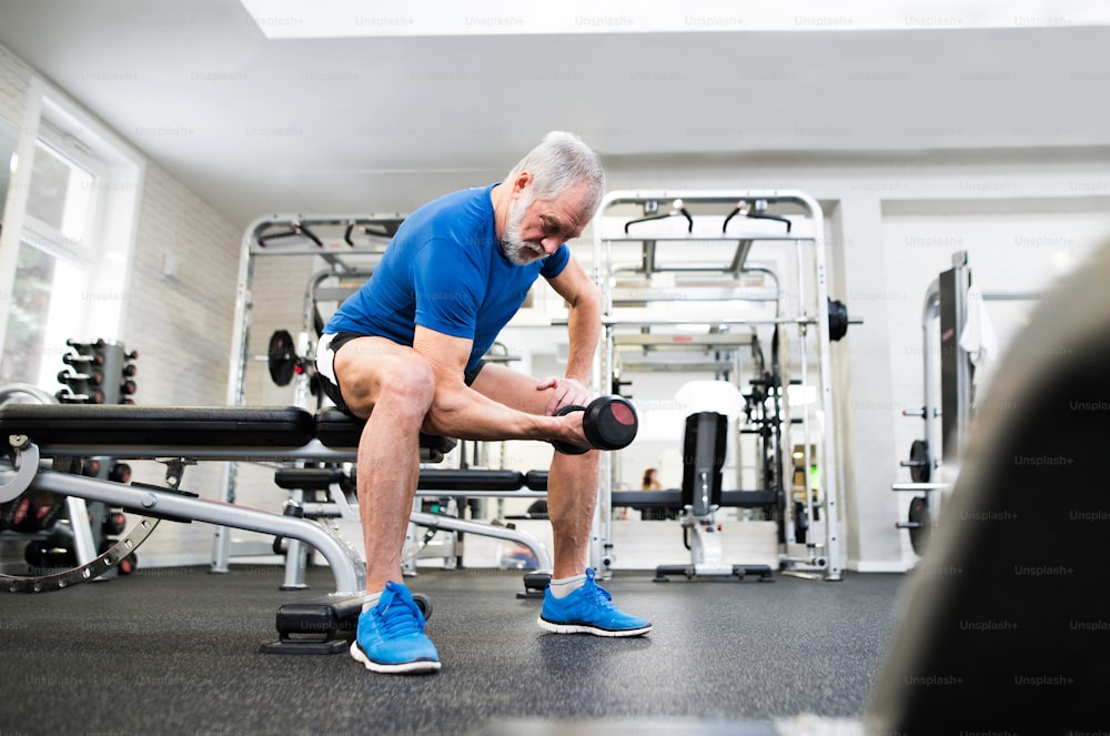 Hombre mayor con ropa deportiva en el gimnasio haciendo ejercicio con pesas.