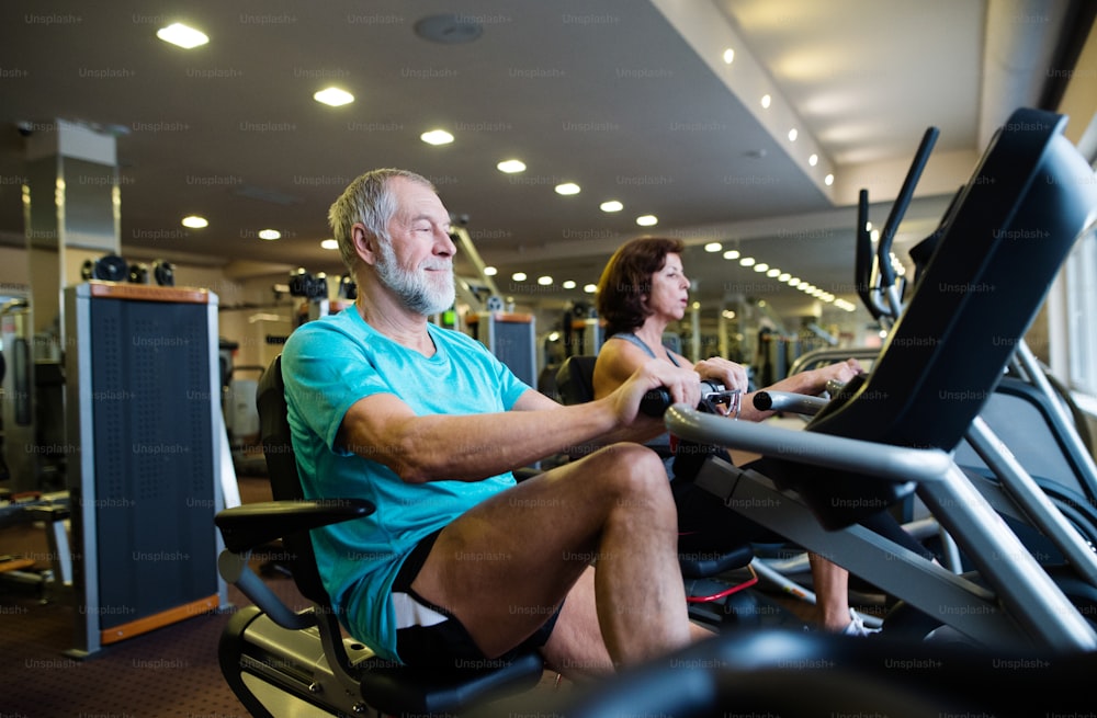 Casal idoso em forma bonita em roupas esportivas na academia fazendo treino cardiovascular, exercitando-se em bicicleta reclinada. Conceito de fitness desportivo e estilo de vida saudável.