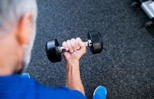 Unrecognizable senior man in sports clothing in gym working out with weights.