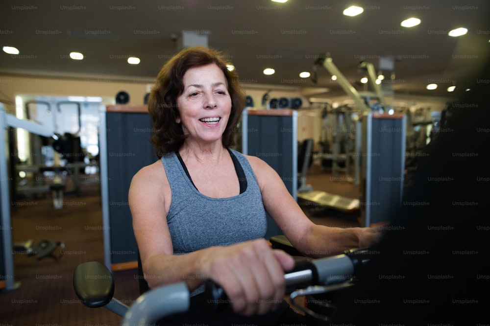 Hermosa mujer mayor en forma con ropa deportiva en el gimnasio haciendo entrenamiento cardiovascular, haciendo ejercicio en bicicleta reclinada. Concepto de fitness deportivo y estilo de vida saludable.
