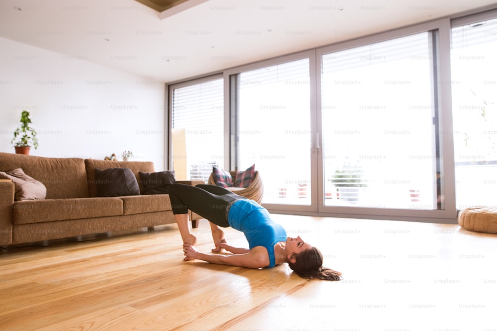 Foto Hermosa mujer joven que hace ejercicio en casa en la sala de estar, haciendo  ejercicio de yoga o pilates. Estiramientos, hacer la postura del puente. –  Leggings Imagen en Unsplash