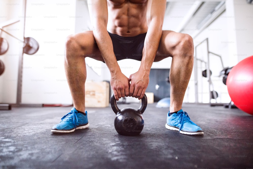 Unrecognizable young fit man doing strength training, doing squats with kettlebell in gym gym