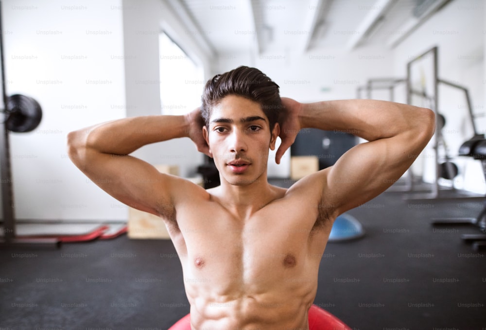 Ajuste o homem hispânico em exercícios de músculos abdominais crunch na bola de fitness durante o treinamento na academia de fitness.