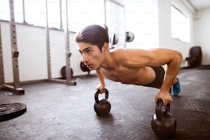 Hombre hispano en forma haciendo entrenamiento de fuerza, haciendo flexiones en pesas rusas en gimnasio gimnasio