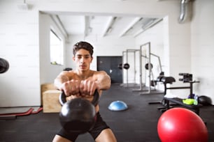 Fit hispanic man doing strength training, doing kettlebell swings in gym gym