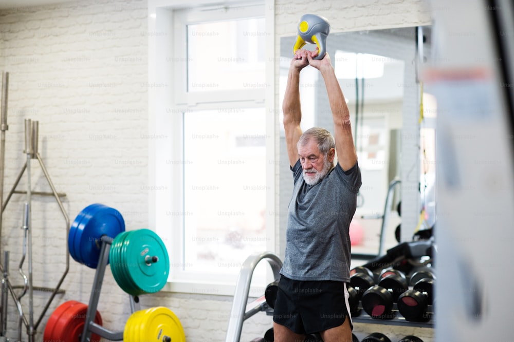 Hombre mayor en forma en el gimnasio haciendo ejercicio con pesas rusas. Concepto de deporte, fitness y estilo de vida saludable.