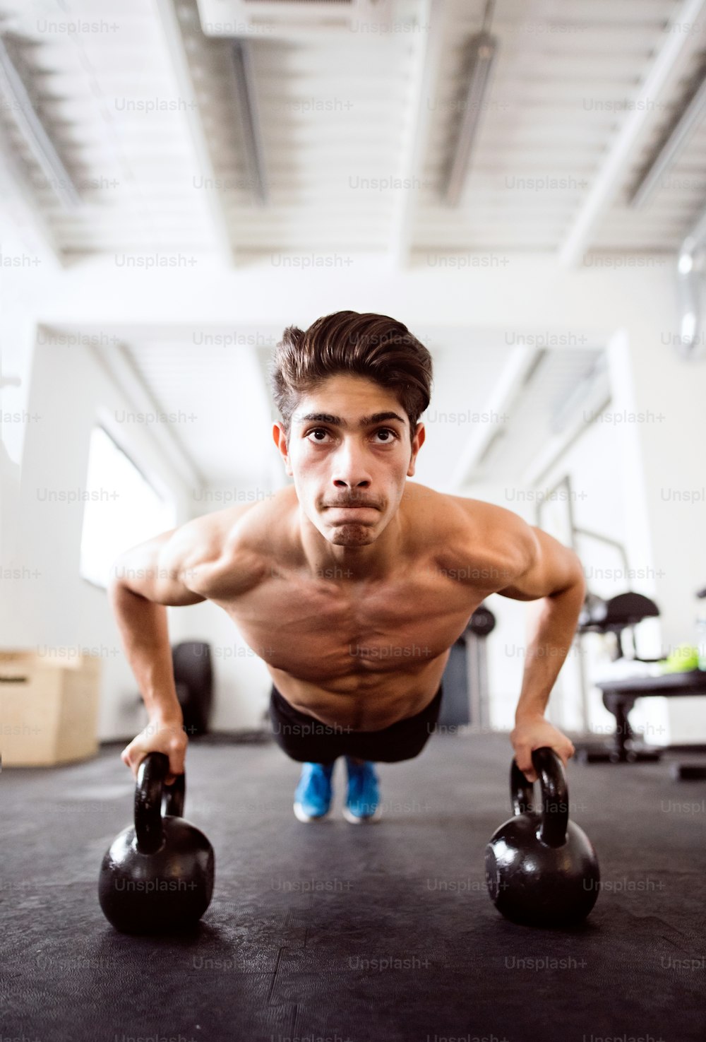 Fit hispanic man doing strength training, doing push ups on kettlebells in gym gym