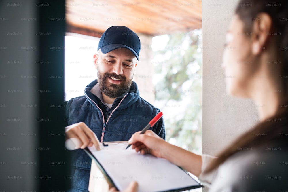 Unrecognizable woman receiving parcel from delivery man at the door - courier service concept.