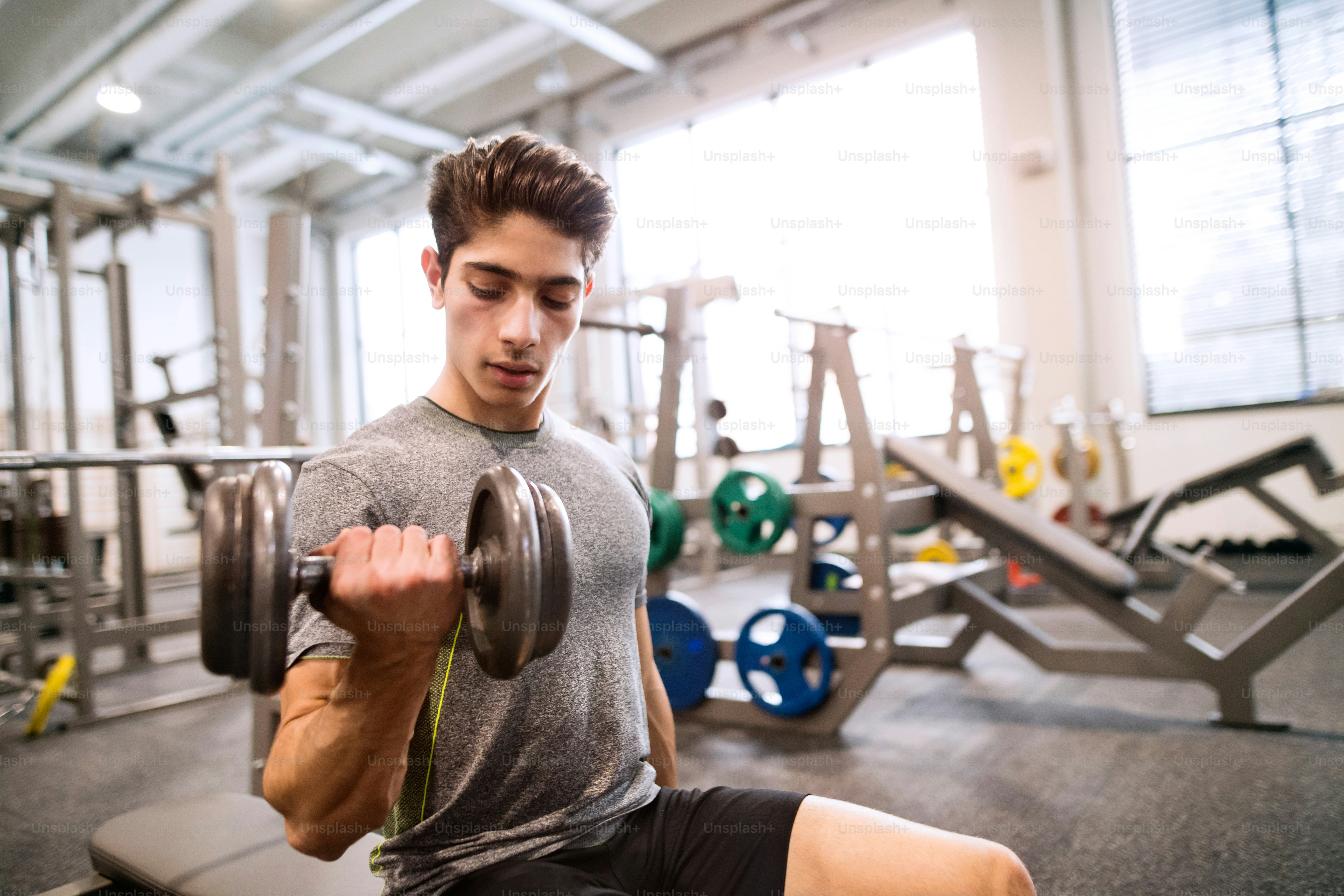 Jeune homme de fitness hispanique dans le gymnase assis sur le banc, s’entraînant avec des poids