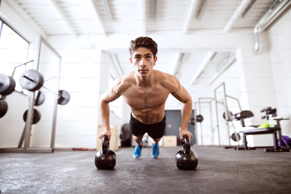 Fit hispanic man doing strength training, doing push ups on kettlebells in gym gym