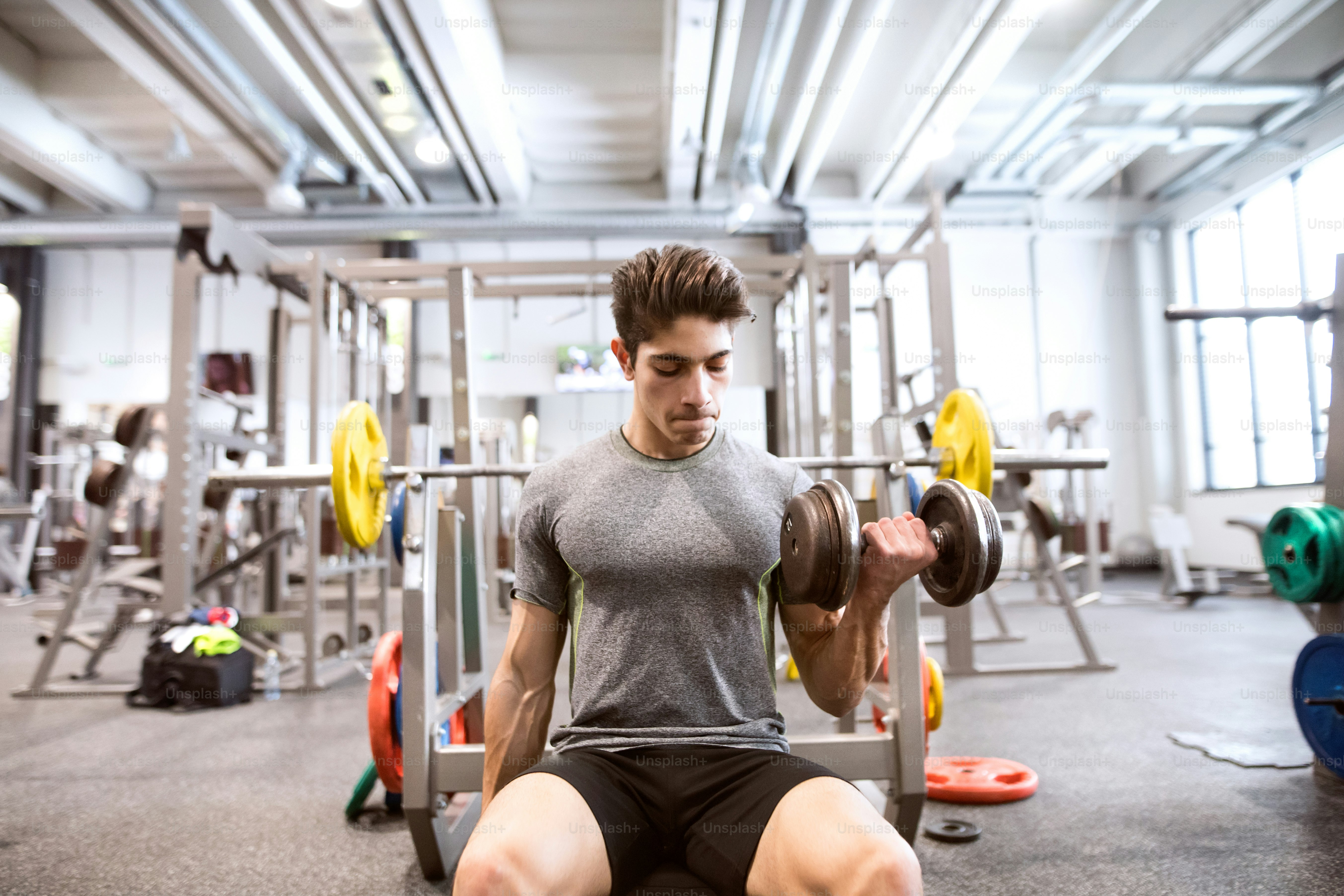 Jeune homme de fitness hispanique dans le gymnase assis sur le banc, s’entraînant avec des poids