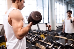 Jeune homme de fitness hispanique dans la salle de sport devant le miroir, s’entraînant avec des poids