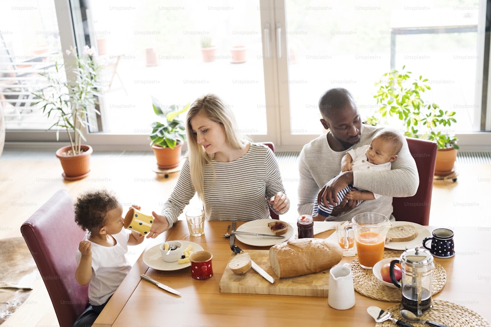 Bella giovane famiglia interrazziale a casa con la loro figlia carina e il figlioletto che fanno colazione insieme.