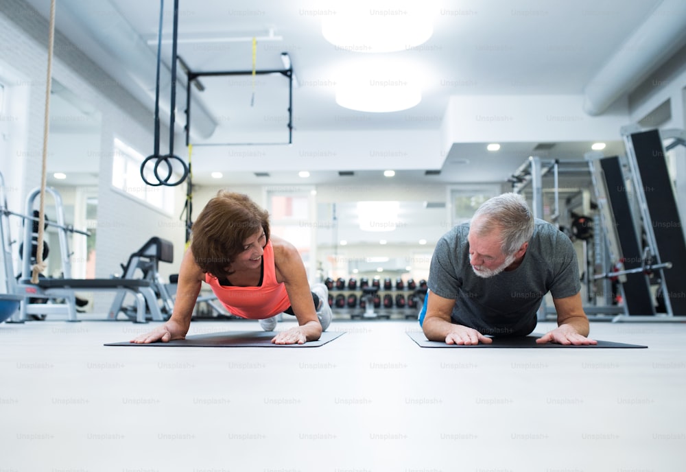 Beautiful fit senior couple in gym in plank position working out abs