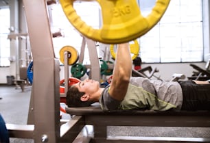 Young hispanic fitness man in gym working out, flexing muscles and making bench press in gym
