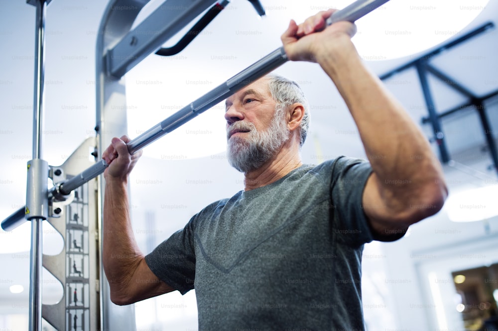 Hombre mayor en forma con ropa deportiva en el gimnasio haciendo ejercicio, haciendo dominadas en la barra horizontal.