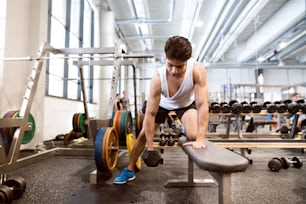 Jeune homme de fitness hispanique dans la salle de sport sur le banc, s’entraînant avec des poids
