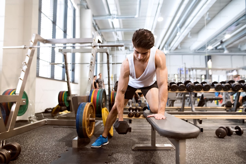 Young hispanic fitness man in gym on bench, working out with weights