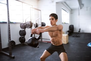 Fit hispanic man doing strength training, doing kettlebell swings in gym gym