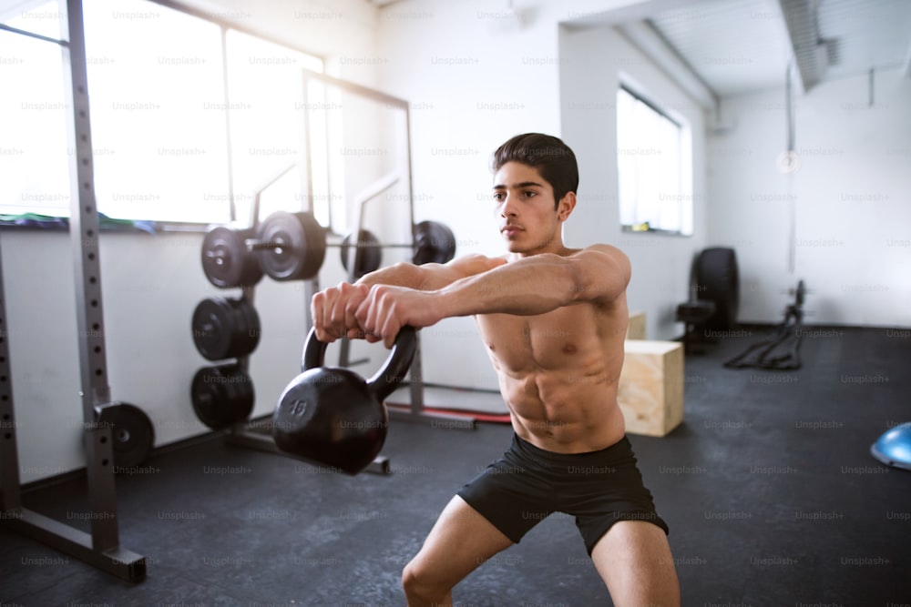 Fit hispanic man doing strength training, doing kettlebell swings in gym gym