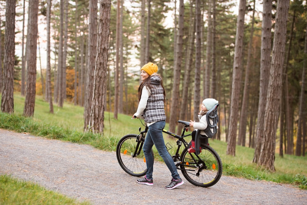 Beautiful young mother with her daughter in warm clothes on bicycle outside in autumn nature