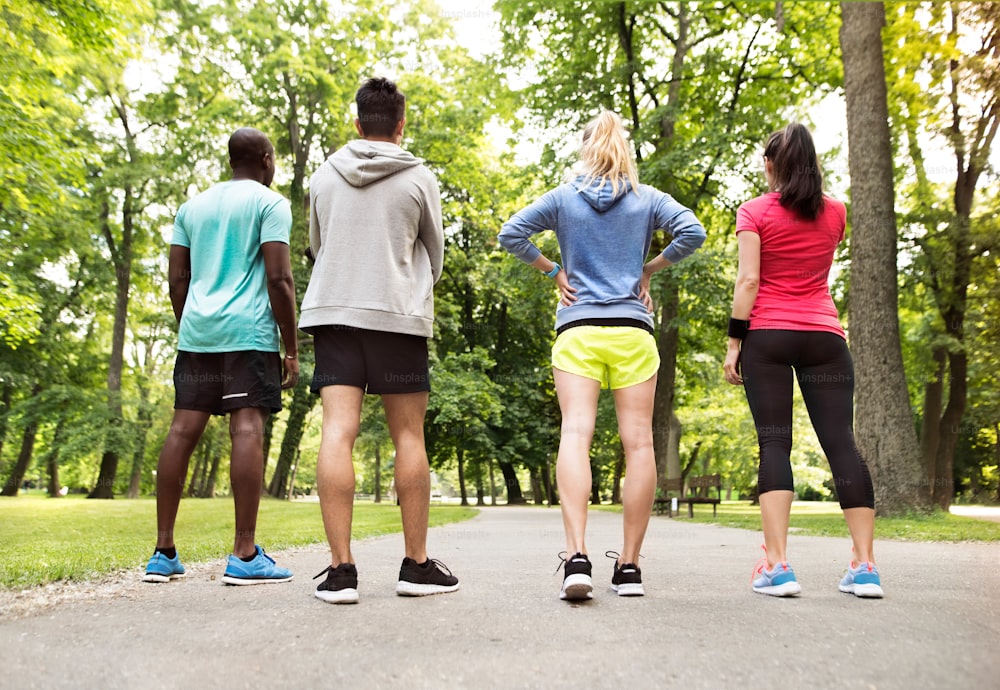 Grupo de jóvenes atletas se preparó para correr en el parque verde y soleado del verano, vista trasera.
