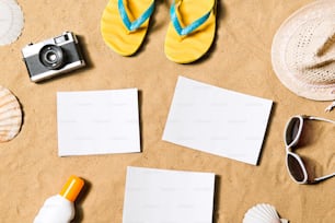 Summer vacation composition with pair of yellow flip flop sandals, hat, sunglasses, sun cream, empty paper sheets and other stuff on a beach. Sand background, studio shot, flat lay. Copy space.