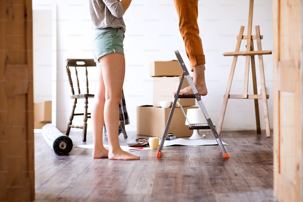 Unrecognizable young married couple moving in new house, man standing on a stepladder, changing a light bulb.