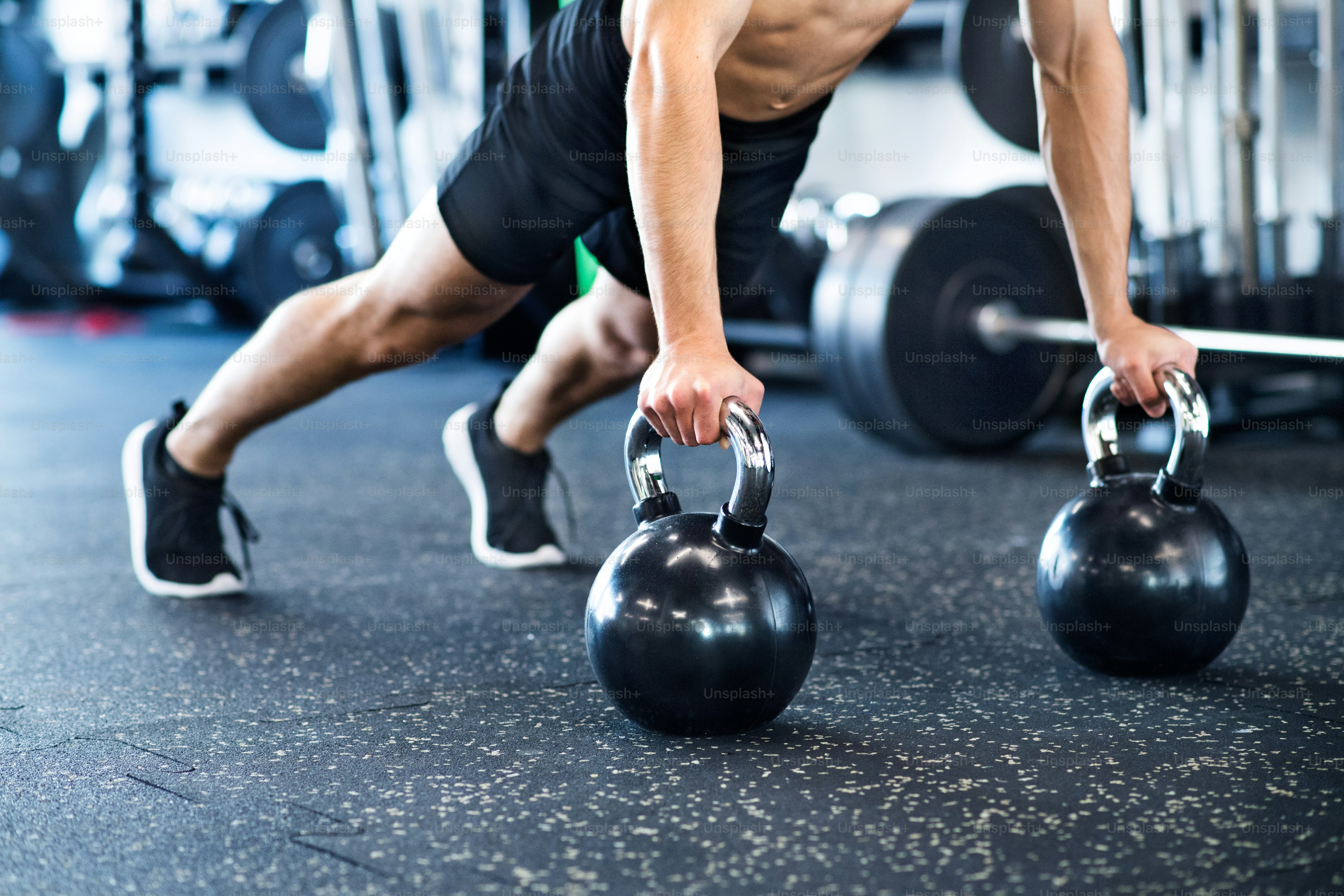 Joven irreconocible en forma haciendo entrenamiento de fuerza, haciendo flexiones en pesas rusas en el gimnasio moderno.