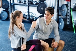 Beautiful young fit couple in modern gym gym doing fist pump.