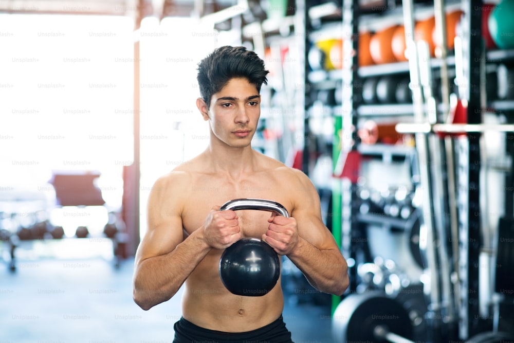 Fit hispanic man doing strength training, exercising with kettlebell in modern gym.