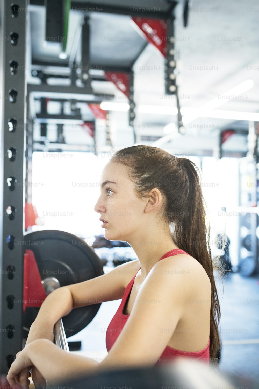Beautiful young fit woman in gym standing at the heavy barbell, resting.