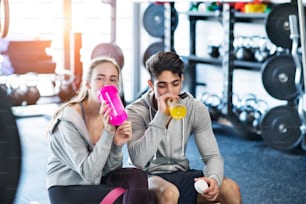Beautiful young fit couple in modern gym gym resting and drinking water.
