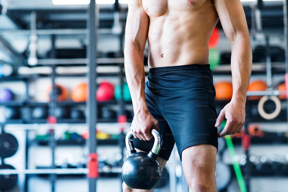 Unrecognizable young fit man doing strength training, exercising with kettlebell in modern gym.