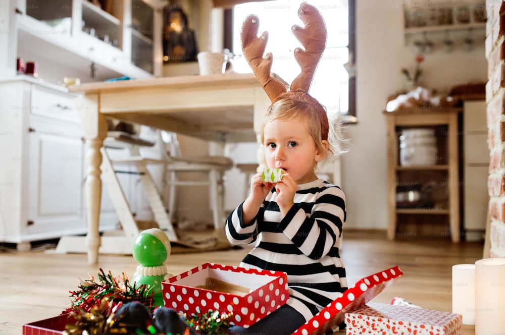 Bambina carina al periodo natalizio che soffia fischi di festa. Figlia che indossa una fascia di renna.