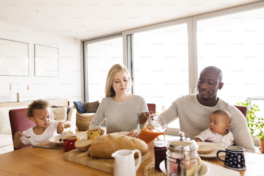 Hermosa joven familia interracial en casa con su linda hija y su pequeño hijo desayunando juntos.