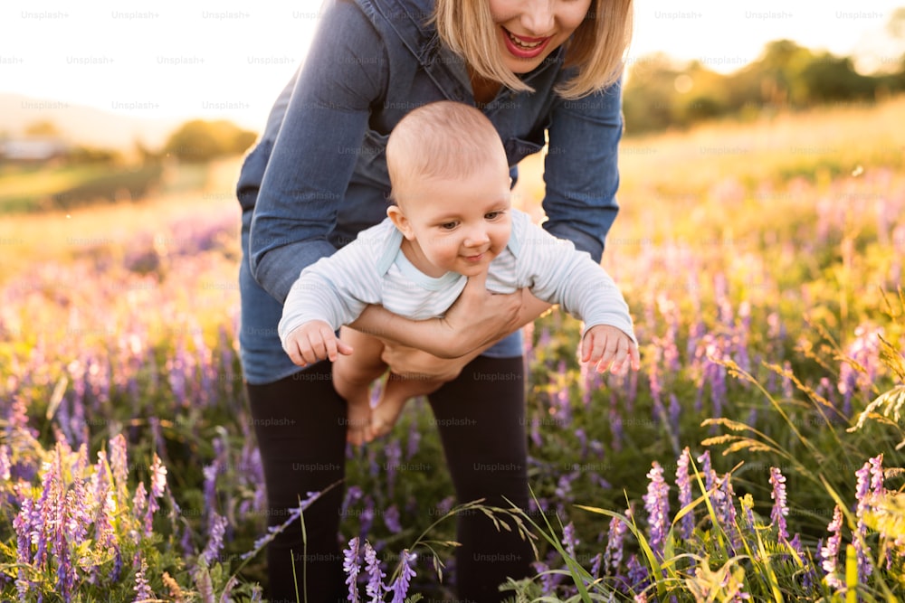 Unkenntliche junge Mutter, die ihren kleinen kleinen Sohn in den Armen hält, draußen in der Natur im Lavendelfeld.