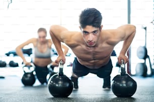 Hermosa pareja joven en forma haciendo entrenamiento de fuerza, haciendo flexiones en pesas rusas en gimnasio moderno