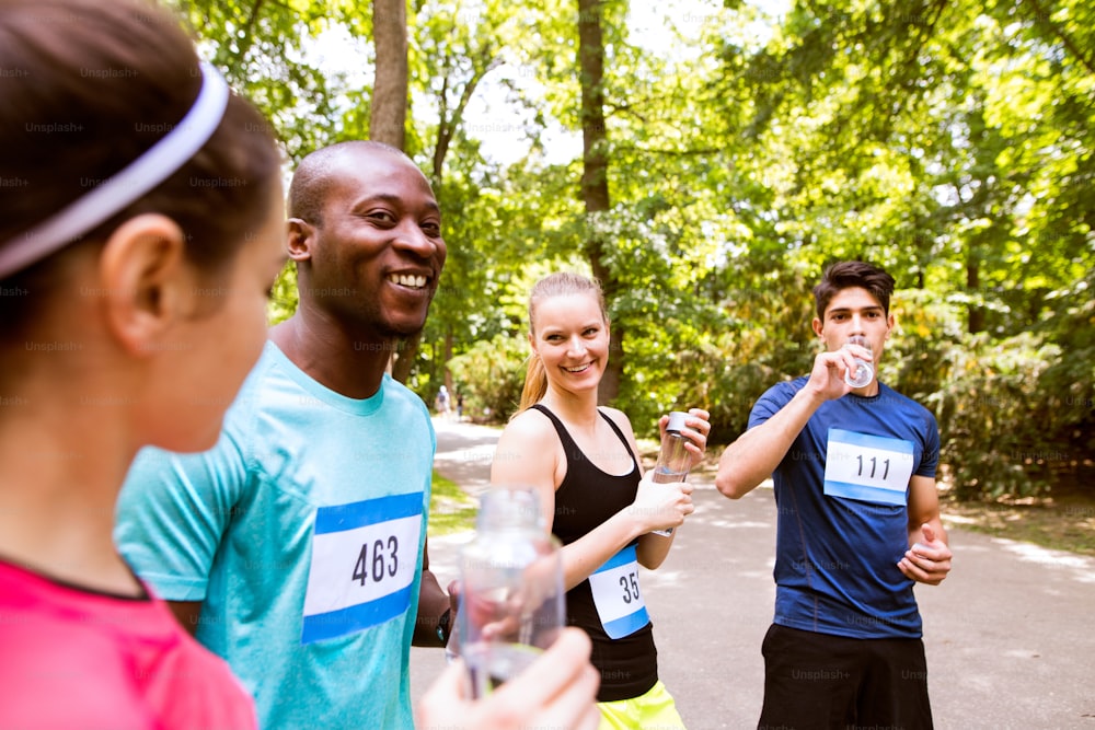 Gruppo di giovani atleti preparati per correre nel parco estivo verde e soleggiato, tenendo bottiglie, acqua potabile.