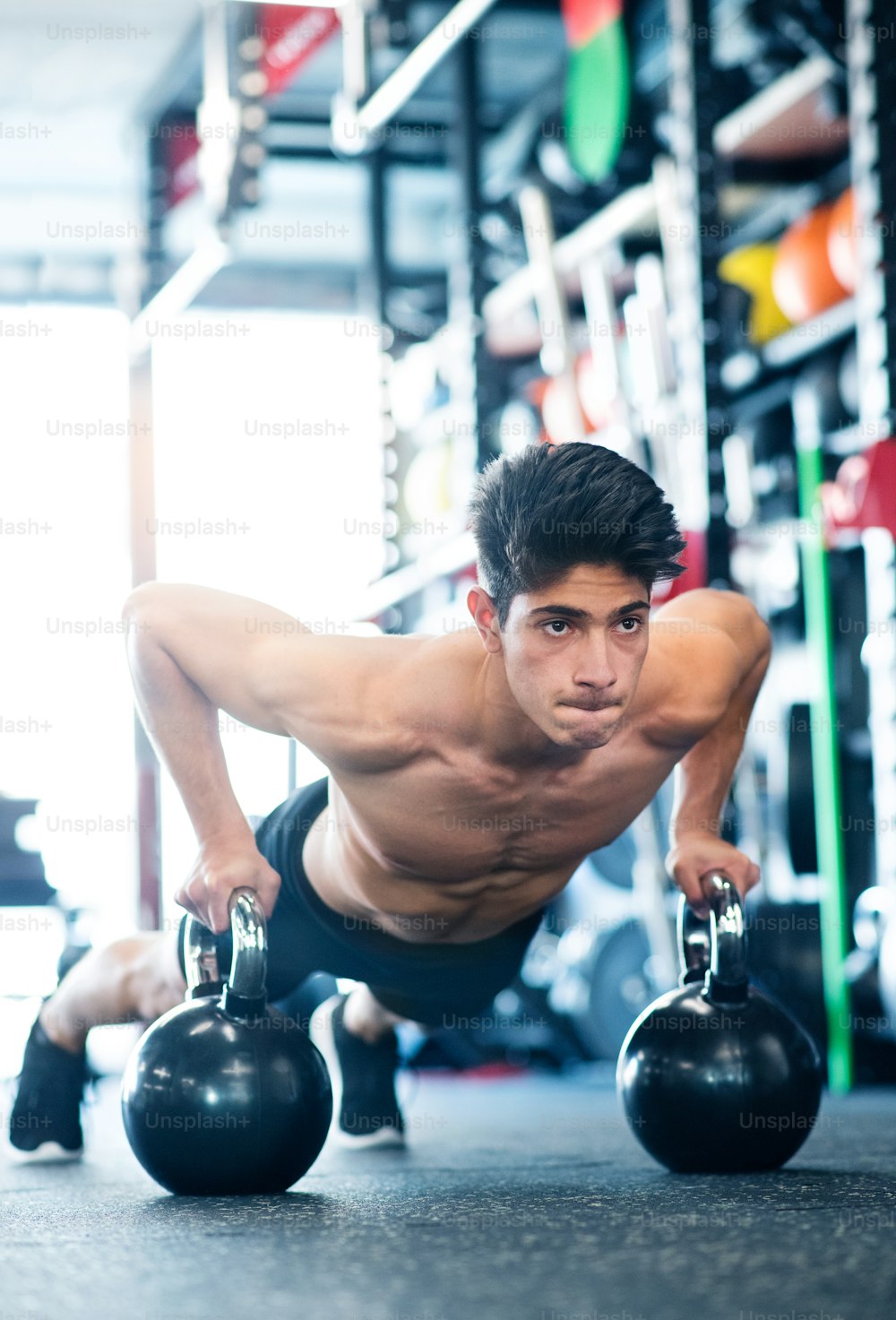 Fit hispanic man doing strength training, doing push ups on kettlebells in modern gym