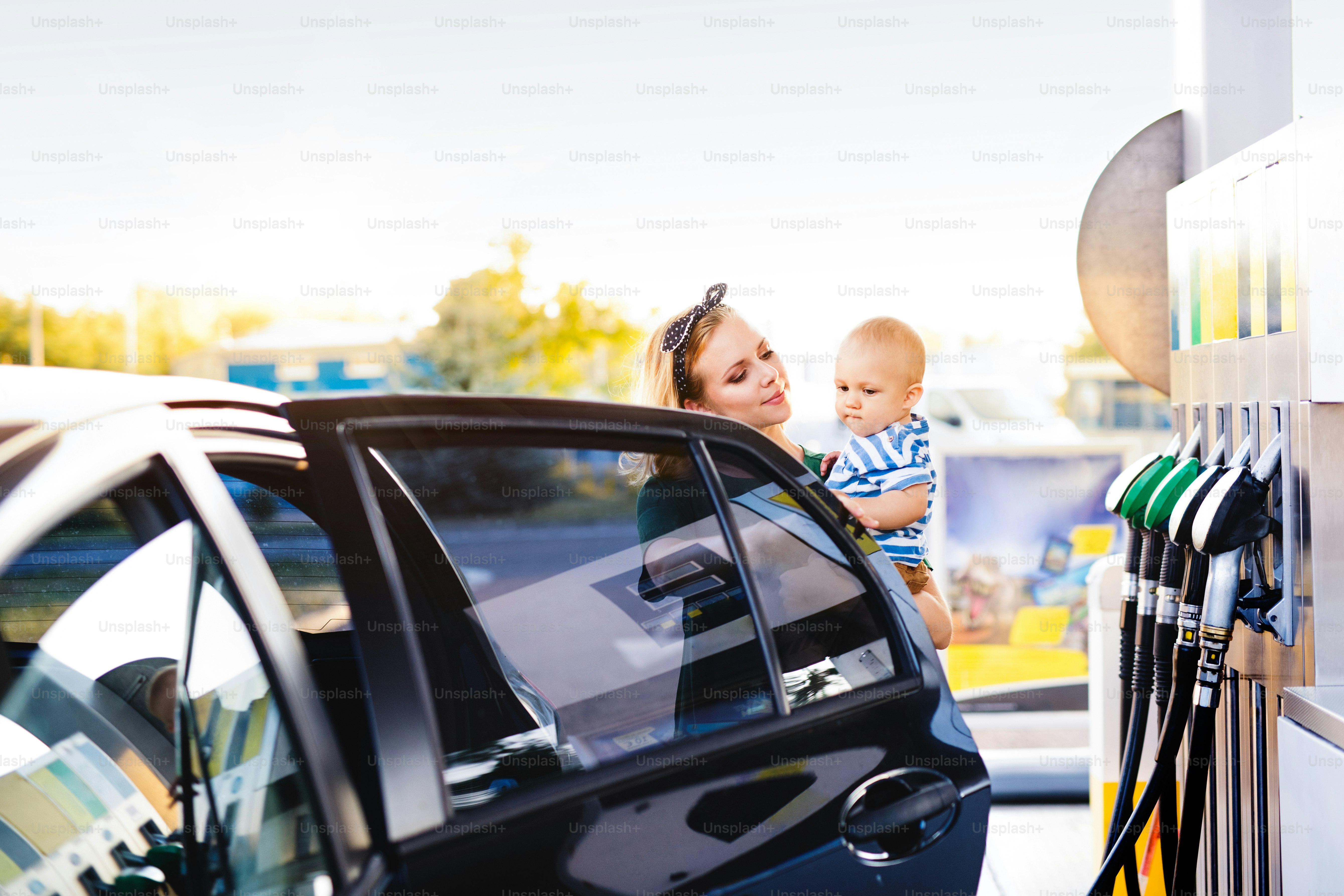 Young mother with baby boy at the petrol station going to refuel the